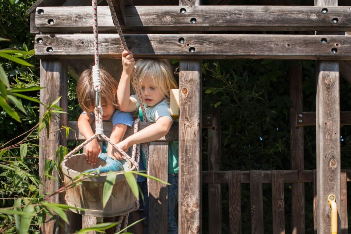 Kinder die in einem Baumhaus einem Korb an einem Seil nach oben ziehen